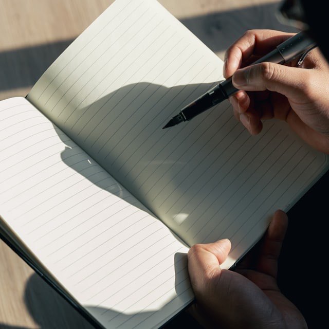 Hands writing in an open lined notebook in warm afternoon sunlight