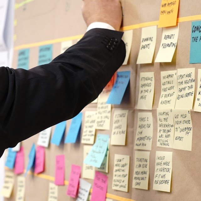A workshop wall covered in handwritten sticky notes, with a facilitator adding another